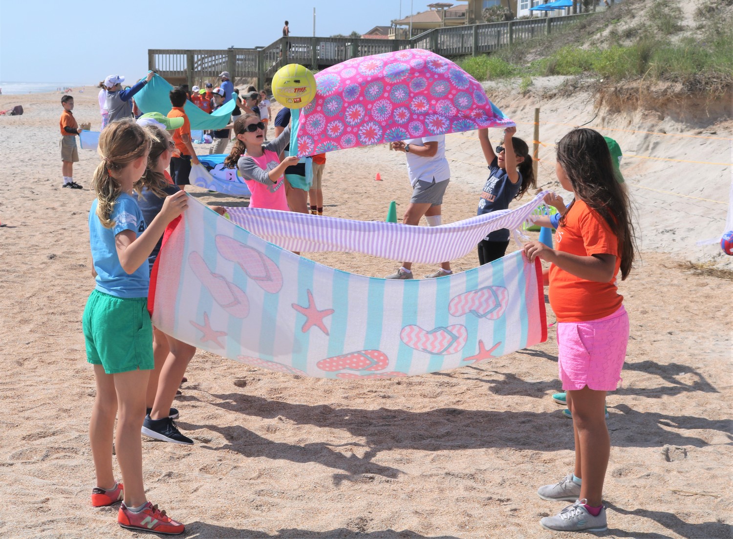 Kids use beach towels to toss volleyballs back and forth.